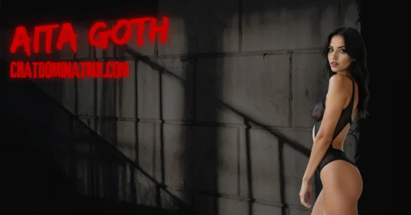 Dominatrix Aita Goth in black lingerie against dungeon wall, representing femdom watersports, humiliation, and submissive baptism through piss play