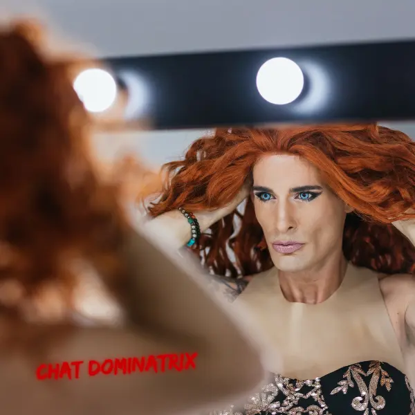 A person with striking red hair and bold makeup gazes into the mirror, capturing the emotional and psychological depth of sissification