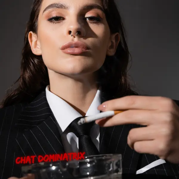 A powerful woman in a sharp pinstripe suit holds a cigarette between her fingers, exuding dominance with a piercing gaze. Her septum piercing and perfectly lined lips add to the aura of control and seduction. This image captures the essence of smoking fetish in BDSM, financial domination, and the intoxicating allure of a powerful femme smoking domme